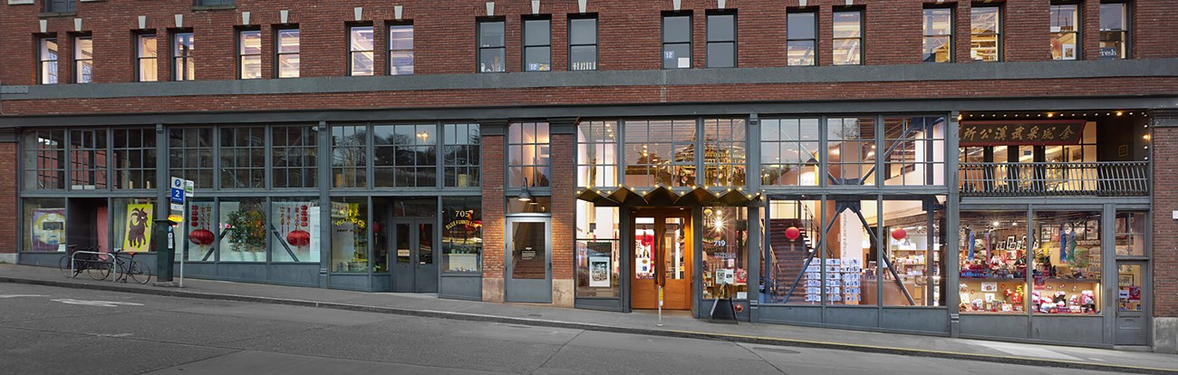 Brick building store fronts on a street with windows filled with various items.