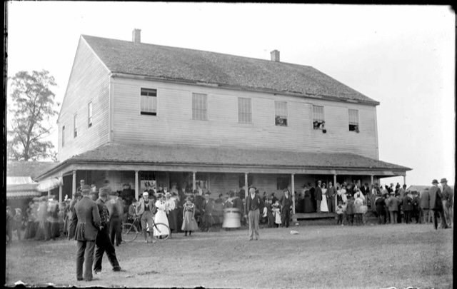 A large plain building surrounded by people in a historic photograph.