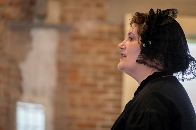 A woman in a black bonnet speaking.