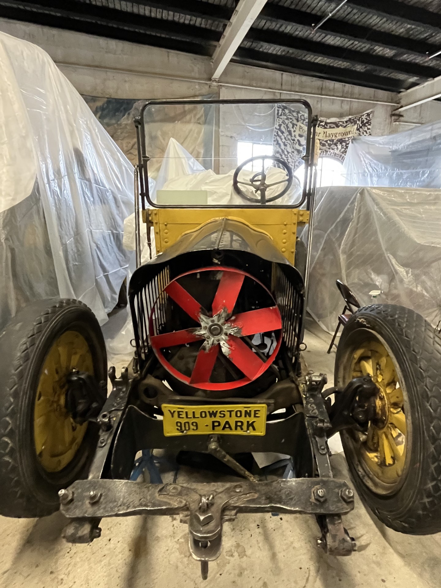 Historic vehicle parked in storage surrounded by protective tarp.