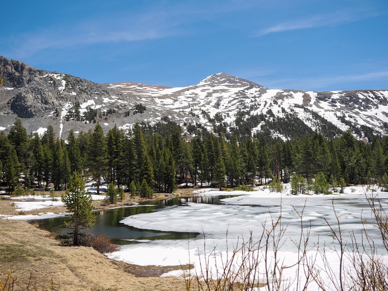 Snowy peak rising above a pond that is still mostly covered in ice