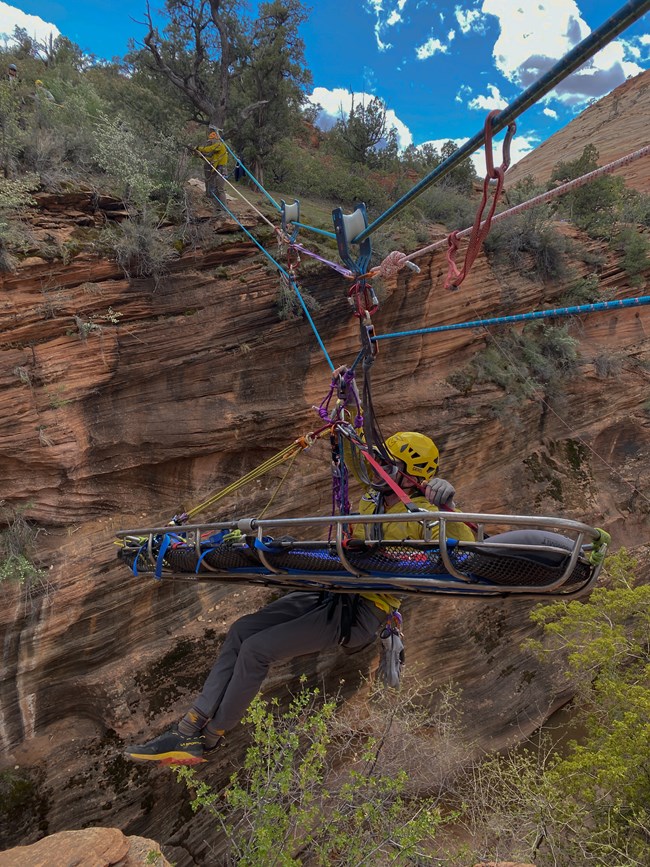 NPS staff move with litter on a rope over a simulated patient during a training exercise.